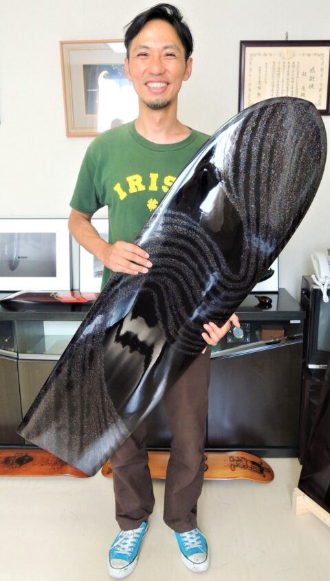 漆塗りのサーフボードを持った堤卓也さん
